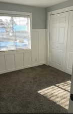 Unfurnished bedroom featuring a decorative wall, dark carpet, wainscoting, and a closet