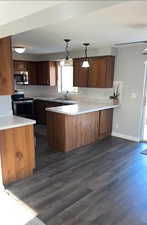 Kitchen featuring light countertops, a peninsula, hanging light fixtures, appliances with stainless steel finishes, and dark wood-style flooring