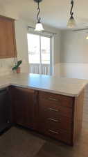 Kitchen with light countertops, pendant lighting, a peninsula, dishwasher, and dark wood-style flooring