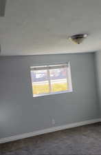 Empty room with baseboards and dark carpet