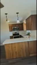 Kitchen featuring light countertops, rail lighting, brown cabinets, hanging light fixtures, and appliances with stainless steel finishes