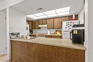 Kitchen featuring white appliances, light countertops, brown cabinetry, estacked washer and dryer, and under cabinet range hood