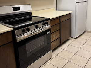 Kitchen with stainless steel range with electric cooktop, dark brown cabinetry, freestanding refrigerator, under cabinet range hood, and light countertops