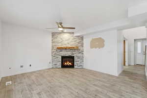 Unfurnished living room with ceiling fan, light wood-style floors, and a stone fireplace