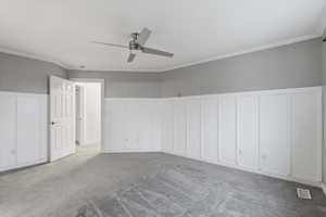 Carpeted empty room with a wainscoted wall, a decorative wall, crown molding, and a ceiling fan