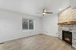 Unfurnished living room featuring a stone fireplace, light wood-style flooring, and ceiling fan