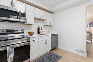 Kitchen with appliances with stainless steel finishes, white cabinets, light wood-type flooring, and light stone counters