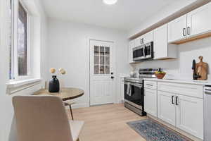 Kitchen featuring appliances with stainless steel finishes, white cabinets, and light wood-type flooring