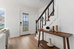 Foyer with light wood-style floors, crown molding, and stairs