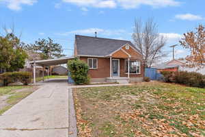 Bungalow featuring brick siding, a carport, driveway, and roof with shingles