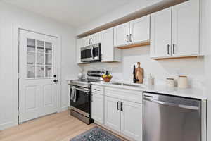 Kitchen with appliances with stainless steel finishes, white cabinets, light wood-style flooring, and light stone countertops