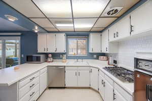 Kitchen featuring light countertops, stainless steel appliances, a peninsula, white cabinets, and backsplash