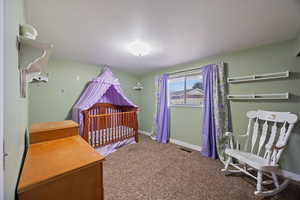 Carpeted bedroom with a crib and baseboards