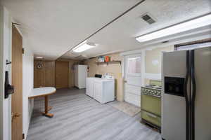 Laundry area featuring a textured ceiling, light wood-type flooring, wooden walls, and washing machine and clothes dryer