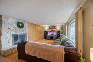 Living room with wood finished floors, wooden walls, a textured ceiling, and a stone fireplace