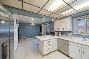 Kitchen featuring stainless steel appliances, white cabinetry, a peninsula, light countertops, and a kitchen bar