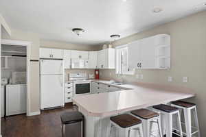 Kitchen featuring light countertops, open shelves, white appliances, and a kitchen bar