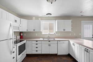 Kitchen with white appliances, white cabinets, light countertops, and a textured ceiling