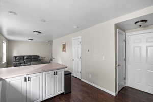 Kitchen with light countertops, white cabinetry, dark wood-style floors, a textured ceiling, and open floor plan