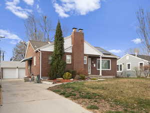 View of front facade featuring brick siding, a chimney, a front lawn, and roof with shingles