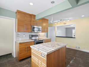 Kitchen featuring brown cabinets, appliances with stainless steel finishes, backsplash, a center island, and decorative light fixtures