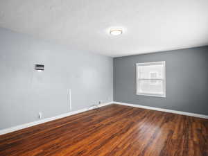 Empty room featuring dark wood-style flooring and a textured ceiling