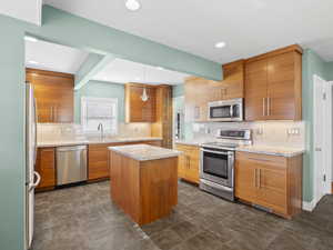 Kitchen with appliances with stainless steel finishes, light stone counters, decorative light fixtures, brown cabinetry, and tasteful backsplash