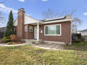 View of front of home featuring a chimney, brick siding, and solar panels