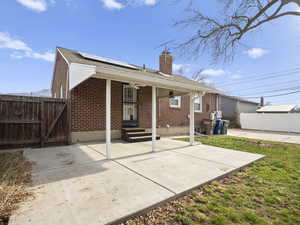 Rear view of property with a gate, roof mounted solar panels, a patio, brick siding, and a chimney