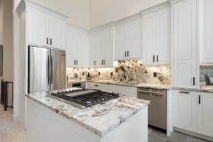 Kitchen with stainless steel appliances, a center island, light stone counters, and white cabinets