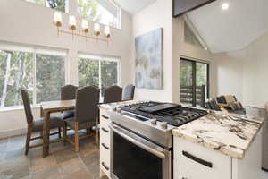 Kitchen with stainless steel range with gas cooktop, white cabinets, high vaulted ceiling, light stone countertops, and stone tile floors