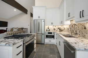 Kitchen featuring stainless steel appliances, light stone countertops, white cabinetry, stone finish flooring, and recessed lighting