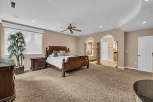 Bedroom with light colored carpet, arched walkways, recessed lighting, and a ceiling fan