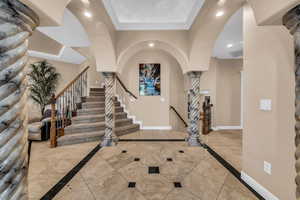 Foyer with inlaid floor details, decorative columns, arched walkways, recessed lighting, and stairway