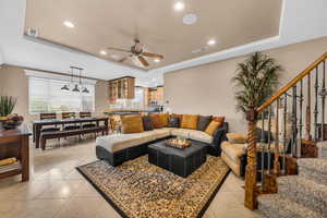 Living room featuring a raised ceiling, recessed lighting, light tile patterned floors, and a ceiling fan
