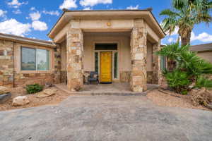 Doorway to property featuring stone siding, covered porch, and stucco siding