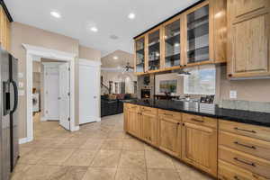 Kitchen featuring dark stone counters, glass insert cabinets, black refrigerator with ice dispenser, open floor plan, and recessed lighting