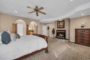 Carpeted bedroom featuring a ceiling fan, a tiled fireplace, arched walkways, and recessed lighting