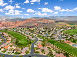 Aerial view of property and surrounding area featuring mountains, a golf club, and nearby suburban area