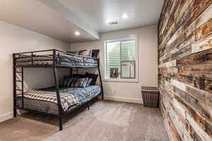 Bedroom with light colored carpet, wooden walls, a textured ceiling, and recessed lighting