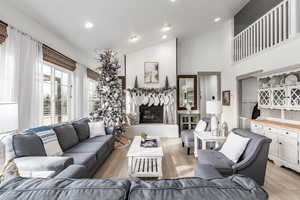 Living area with light wood-type flooring, high vaulted ceiling, a large fireplace, and recessed lighting