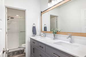 Full bathroom featuring double vanity, a stall shower, and dark wood-style flooring