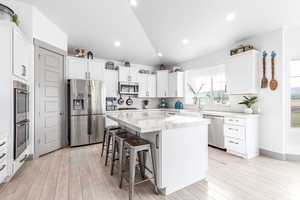 Kitchen featuring vaulted ceiling, a kitchen bar, stainless steel appliances, white cabinetry, and a kitchen island