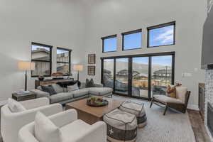 Living room with a stone fireplace, wood finished floors, and a towering ceiling