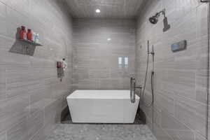 Full bath featuring a freestanding tub, tiled shower, and tile walls