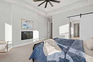 Bedroom featuring a barn door, light colored carpet, ceiling fan, a glass covered fireplace, and recessed lighting