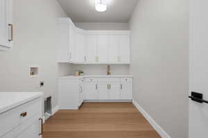 Laundry area with cabinet space, light wood finished floors, washer hookup, and hookup for an electric dryer