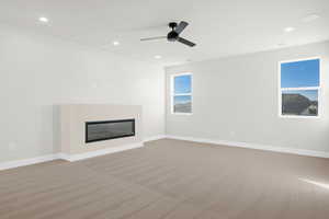 Unfurnished living room featuring a glass covered fireplace, light carpet, recessed lighting, and a ceiling fan