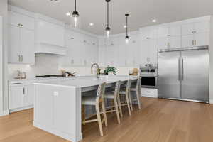 Kitchen with stainless steel appliances, white cabinetry, pendant lighting, an island with sink, and a breakfast bar area