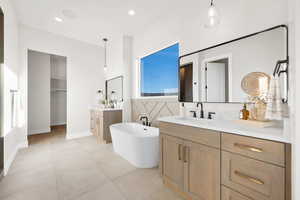 Full bathroom with a freestanding bath, two vanities, a walk in closet, light tile patterned floors, and recessed lighting